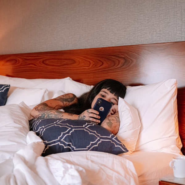 image of a woman laying in a hotel bed looking at her phone